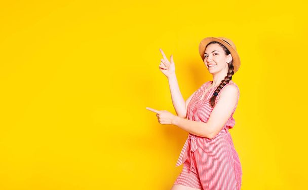 Sarı bir duvara yaslanmış mutlu genç bir kadının fotoğrafı. Uzayın nereyi gösterdiğini gösteren kameraya bakıyoruz.. - Fotoğraf, Görsel