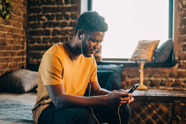 Black young man listening to music otr telecoference on mobile phone - Фото, зображення