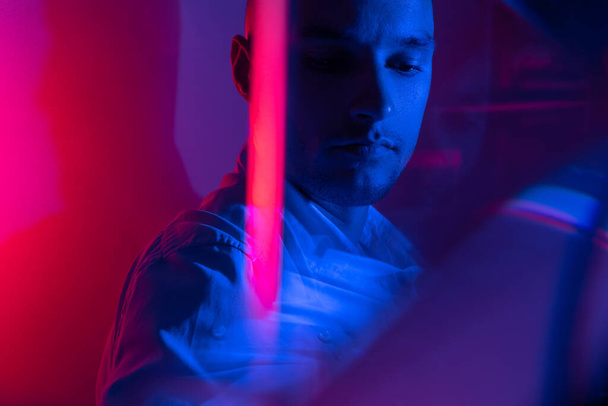Close-up cinematic portrait of handsome young man in neon blue pink lighted room, stylish male model indoors. Reflection effect - Foto, Bild