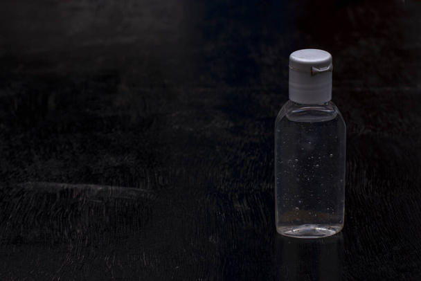 A bottle of sanitizer with a cloth musk out of focus on a black background. Selective focus. - Fotoğraf, Görsel