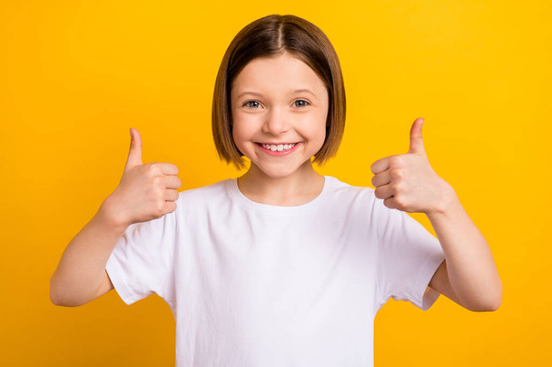 Photo portrait little girl with bob hairdress smiling showing thumb-up gesture isolated vibrant yellow color background - Foto, Imagem