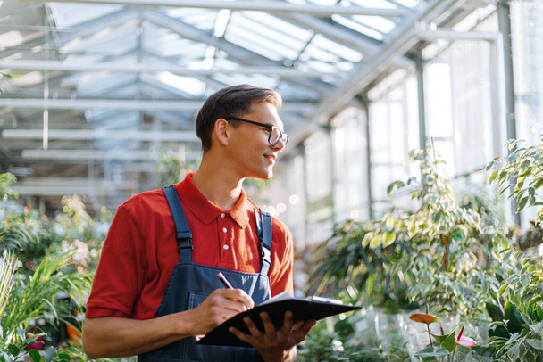 supervisor with clipboard standing near the shelves with a variety of plants . - 写真・画像