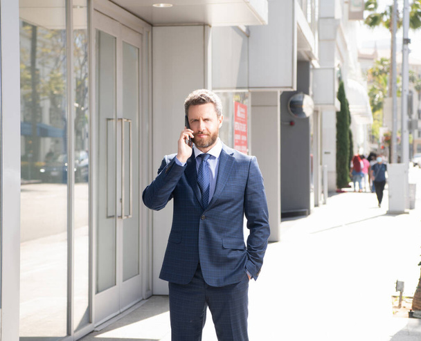 зрілий чоловік бізнесмен у діловому костюмі говорить по телефону за межами офісу, спілкування
 - Фото, зображення