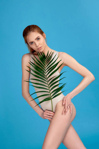 mujer con cuerpo perfecto en traje de cuerpo sosteniendo hojas de palma - Foto, imagen