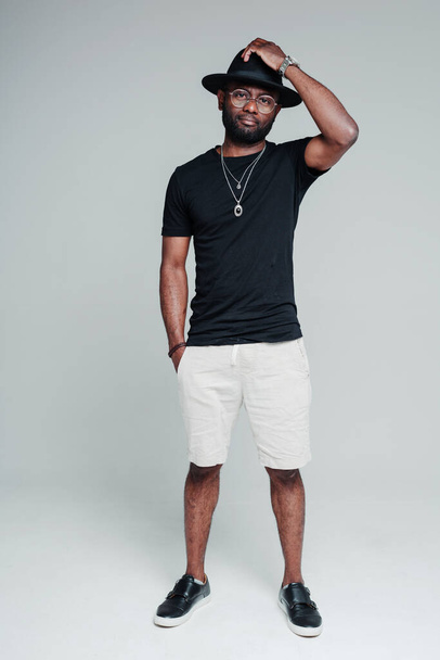 Handsome african american man in shorts and a t-shirt putting a hat on his head - Foto, Bild