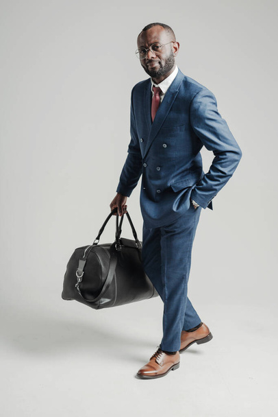 African American businessman in a suit holds a bag with things in his hand and is going on a business trip - Photo, Image