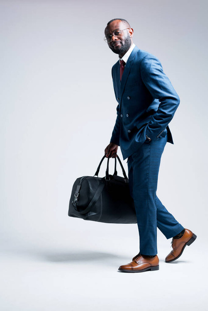 African American businessman in a suit holds a bag with things in his hand and is going on a business trip - Fotó, kép