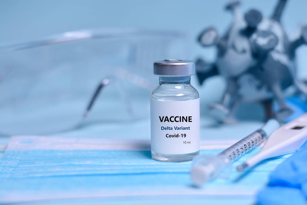 Due flaconi di vaccino Covid-19 per immunizzare dalla variante Delta Coronavirus, siringa, maschera facciale, termometro per il corpo e occhiali protettivi su fondo blu. Il concetto di medicina, sanità - Foto, immagini