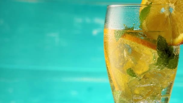Традиционный холодный летний коктейль, сделанный из газированной воды, нарезанного апельсина и мяты, вращающийся на синем фоне. - Кадры, видео