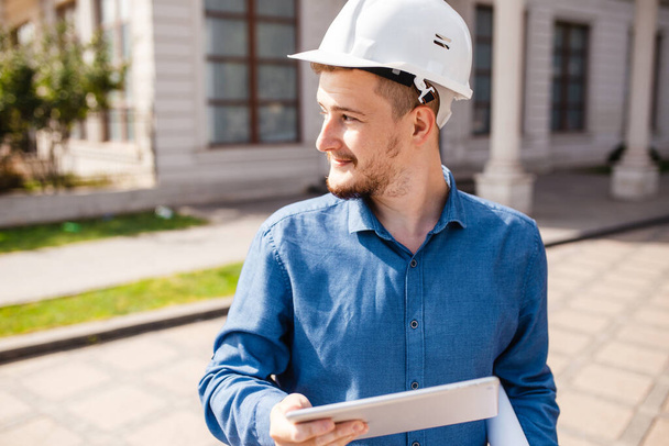 Ein Ingenieur oder Architekt mit Helm und Tablet in der Hand. Überwachung des Baufortschritts. Ein Mann mit hartem Hut - Foto, Bild