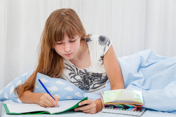 The girl does homework at home on the bed. Distance learning. Lessons. homework. education. - Photo, image