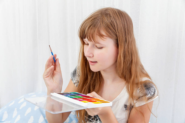 Ξανθιά κοπέλα παίρνει με ένα πινέλο το χρώμα του χρώματος σε μια παλέτα ακουαρέλα. Διαβάζω. εκπαίδευση. Δημιουργικότητα, σχέδιο - Φωτογραφία, εικόνα