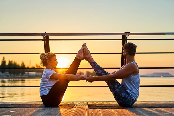 Fit young couple doing acro yoga at pier by the sea. Healthy lifestyle. People outdoor sport activity on family vacation - Foto, Imagem