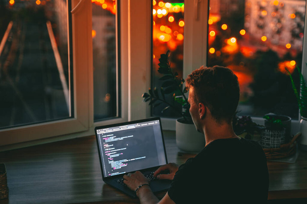 Um jovem desenvolvedor masculino está programando um script de código tarde da noite com belas luzes da cidade à noite - Foto, Imagem