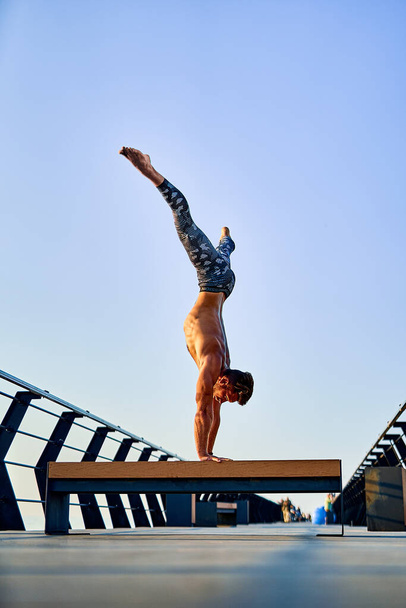 Fit man doing a hand stand while practicing yoga alone near the ocean against sky at dusk or dawn - Fotografie, Obrázek