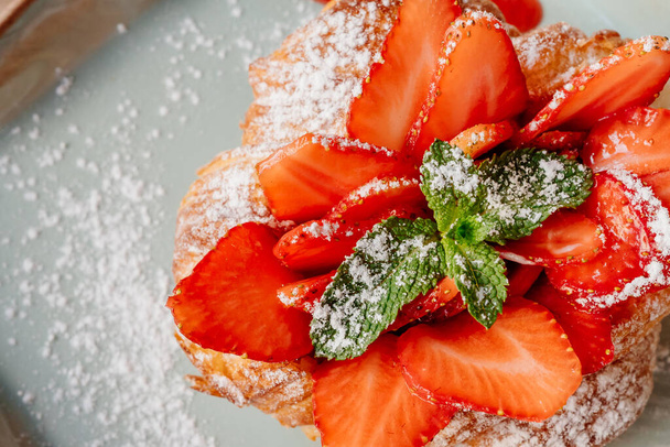 croissant with strawberries, mint and powdered sugar on a white plate. - Фото, зображення