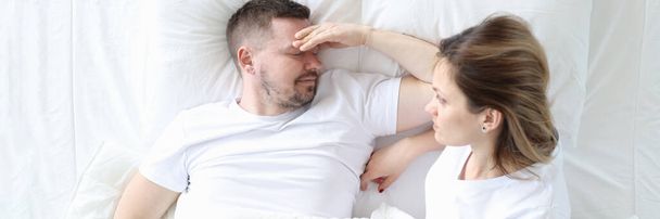 Married couple is lying in bed top view. Man holding his head - Foto, afbeelding