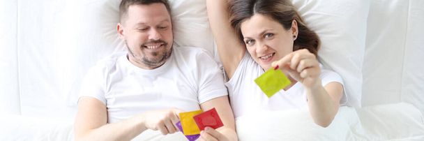 Hombre y mujer acostados en la cama y sosteniendo condones vista superior - Foto, imagen