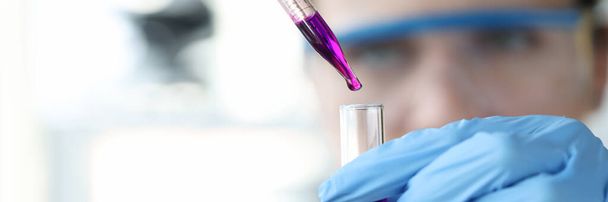Researcher drips purple liquid from pipette into test tube - Фото, изображение