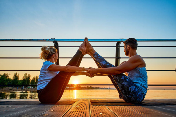 Fit young couple doing acro yoga at pier by the sea. Healthy lifestyle. People outdoor sport activity on family vacation - Fotó, kép