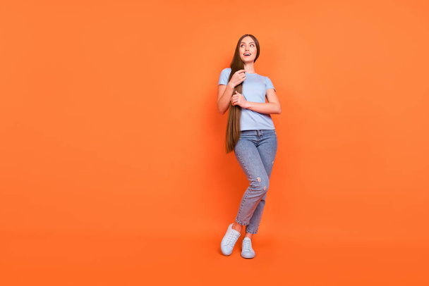 Full size photo of young teen girl happy positive smile hands touch hair look empty space isolated over orange color background - Foto, Imagen