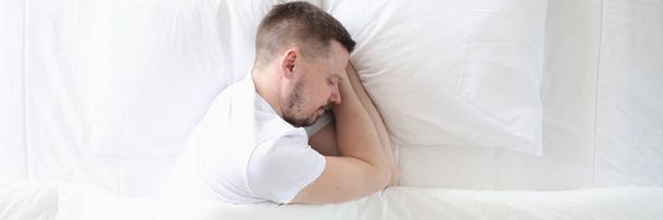 Young man is sleeping peacefully on large white bed - Photo, Image