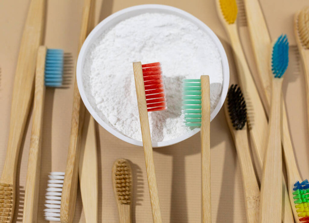 Un conjunto de cepillos de dientes de bambú ecológicos multicolores y polvo de dientes blancos sobre un fondo beige pastel. Desperdicio cero, estilo de vida sostenible. Concepto libre de plástico - Foto, Imagen