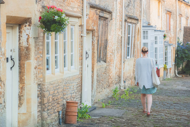 Młoda blondynka turystka odkrywa uroczą wiejską uliczkę w historycznej wiejskiej wiosce Corhsam, w letni wieczór w Cotswolds, Wiltshire, UK. - Zdjęcie, obraz
