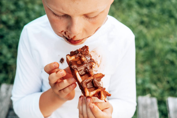 Ребенок ест бельгийские вафли с шоколадной начинкой. Вид сверху. повседневной жизни грязные пятна для стирки и чистой концепции. Высокое качество фото - Фото, изображение