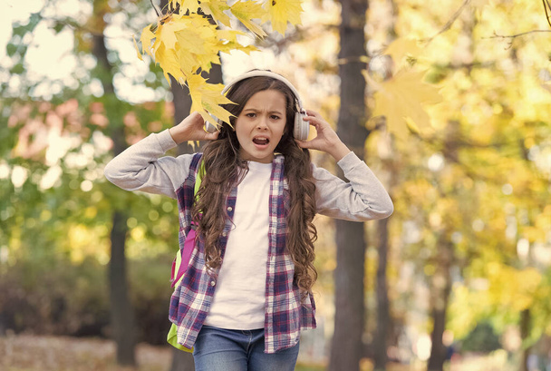 Irritated little girl suffer from loud unpleasant music sound cacophony in autumn park outdoors, headphones - Photo, image