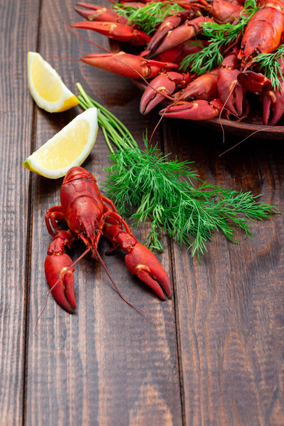 Red crayfishes on a plate served with dill and lemon, on a dark wooden background, vertical, copy space - Фото, зображення
