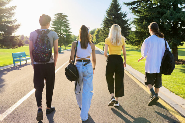 Group of teenage friends on sunny summer day walking together on road, back view - Foto, afbeelding