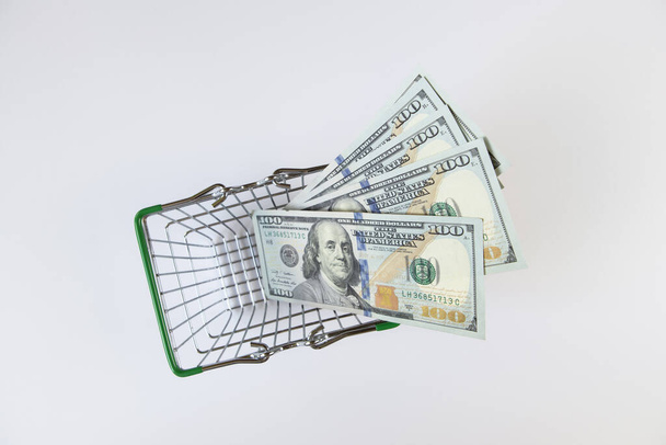 100 dollar bills in a mini shopping basket on a white background, top view, flat lay. Finance concept, buying currency, business. Paper money, offline purchases. Horizontal. - Fotó, kép