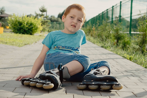 A boy tries to get up from the ground after falling with the roller skates. a boy riding a bike or roller, fell and injured his leg - Foto, imagen