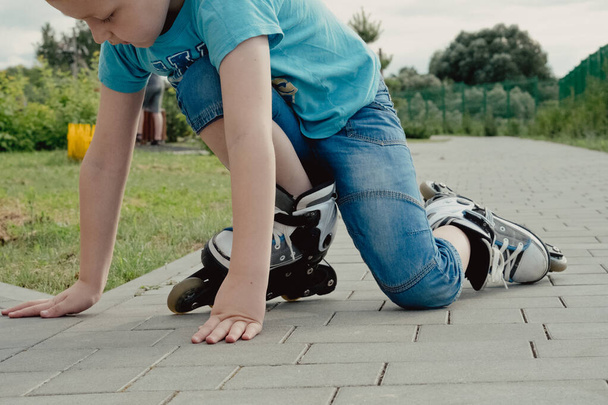 A boy tries to get up from the ground after falling with the roller skates. a boy riding a bike or roller, fell and injured his leg - Foto, afbeelding