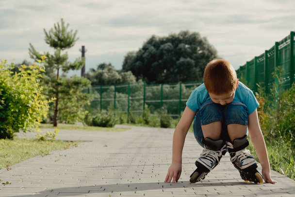 A boy tries to get up from the ground after falling with the roller skates. a boy riding a bike or roller, fell and injured his leg - Φωτογραφία, εικόνα