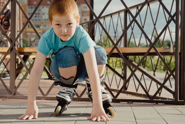 A boy tries to get up from the ground after falling with the roller skates. a boy riding a bike or roller, fell and injured his leg - Fotoğraf, Görsel