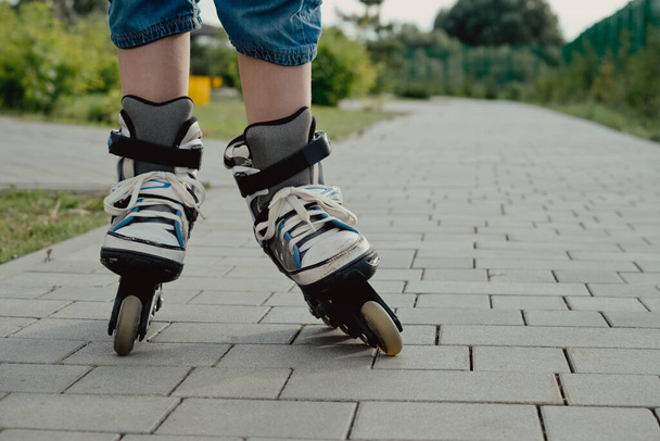 Little boy in protective equipment and rollers stands on walkway in park, low angle view - 写真・画像