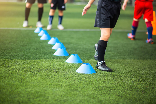 Selectieve focus op kegel marker met wazig kind voetbal wordt uitgevoerd op groene kunstgras. Materiaal voor trainingslessen van de voetbalacademie. - Foto, afbeelding