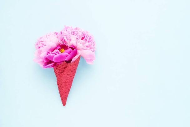 Pink peony flowers in a red waffle ice cream cone on blue background. Mothers Day, Valentines Day, summer concept. - Photo, Image