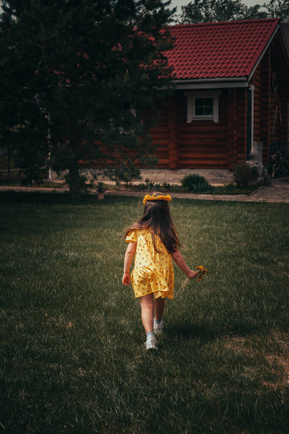 rear view of the back of a running preschool girl in a yellow dress in the backyard on a summer day - Fotografie, Obrázek