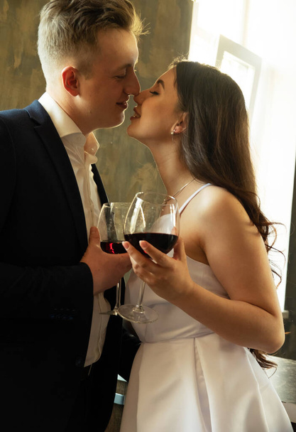 A fiatal házaspár bort iszik és mosolyog boldogságukra, romantikájukra és gyengédségükre. - Fotó, kép