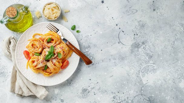Tasty appetizing classic italian tagliatelle pasta with tomato sauce, cheese parmesan and basil on plate on light table. View from above, horizontal. Top view with copy space. - Photo, Image