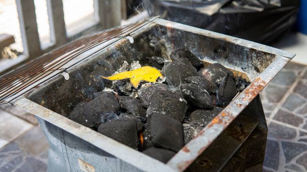 A glowing piles of charcoal briquettes using fire starter inside of black portable mini picnic barbeque grill box. BBQ preparation. - Photo, Image
