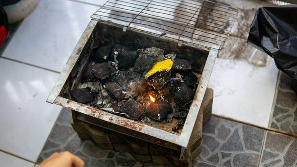 Um brilhante pilhas de briquetes de carvão usando fogo iniciador dentro de preto portátil mini piquenique churrasqueira caixa. Preparação para churrasco. - Foto, Imagem