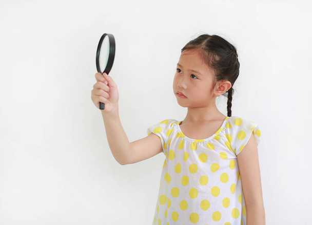 Surprised Asian Kid looking through a magnifying glass to beside on white background - Photo, Image