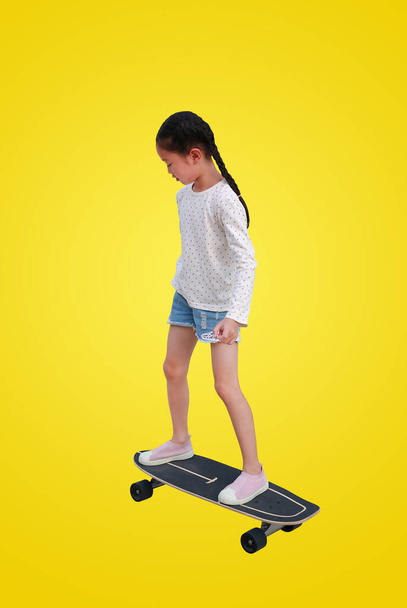 Kleine asiatische Mädchen, die auf einem Skateboard auf gelbem Hintergrund Schlittschuh laufen. Kind fährt auf Skateboard mit Clipping-Pfad - Foto, Bild