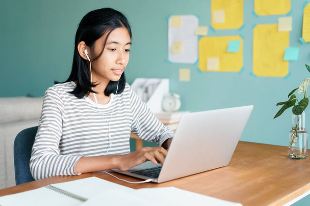 Glückliche asiatische Mädchen Videotelefonie online über Internet-Tutor auf Laptop-Computer mit Kopfhörer, während auf einem Tisch zu Hause sitzen morgens, Konzept Fernunterricht zu Hause - Foto, Bild
