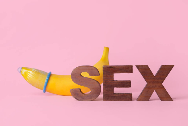 Word SEX and banana in condom on color background - Photo, Image