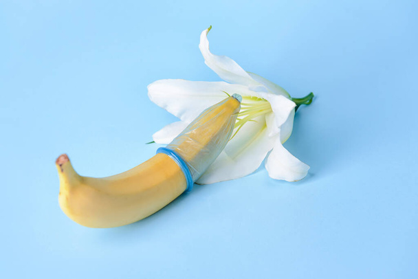 Банана в презервативі і квітці на кольоровому тлі. Еротична концепція - Фото, зображення
